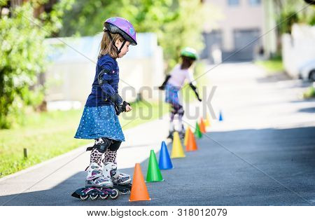 Children Learning To Roller Skate On The Road With Cones.