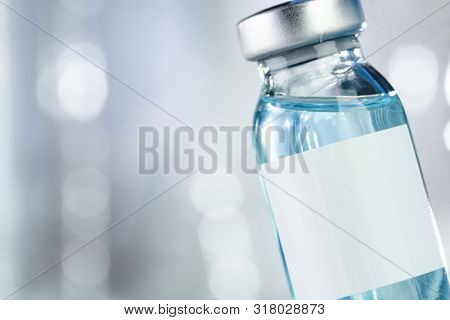 Healthcare concept with a hand in blue medical gloves holding a vaccine vial with blue liquid and black white label