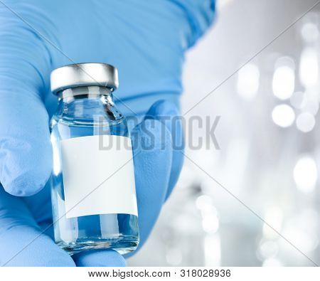 Healthcare concept with a hand in blue medical gloves holding a vaccine vial with blue liquid and black white label