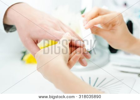 Woman filing fingernails of a man in her nail parlor