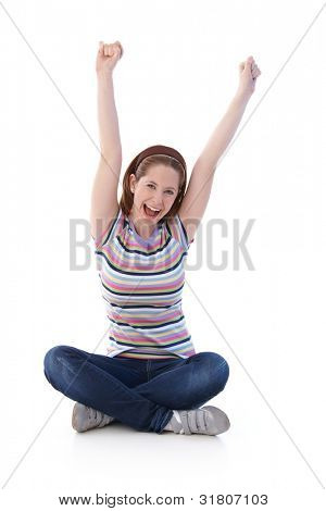 Giovane ragazza seduta sul pavimento nella sede di sarto, stretching mani verso il cielo, gridando allegramente.