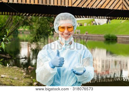 Female Ecologist Or Epidemiologist Gestures For Excellent Quality Of Water, Holding A Flask In One H