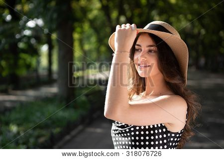 Close-up Porttrait Of A Beautiful Young Brunette Woman Dressed In A Black Dress And A Hat With Wide 