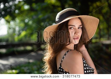 Close-up Porttrait Of A Beautiful Young Brunette Woman Dressed In A Black Dress And A Hat With Wide 