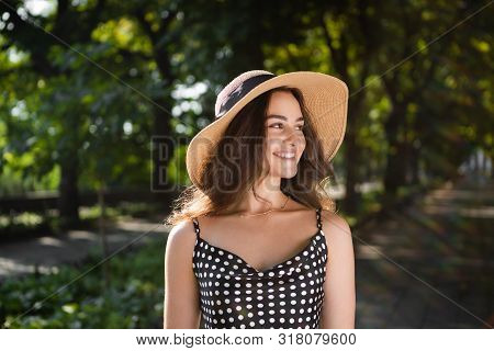 Close-up Porttrait Of A Beautiful Young Brunette Woman Dressed In A Black Dress And A Hat With Wide 