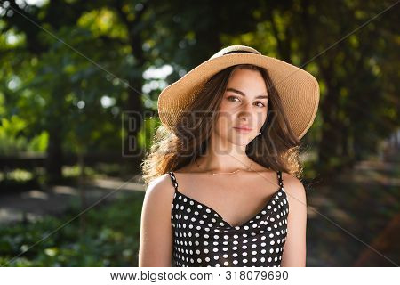 Close-up Porttrait Of A Beautiful Young Brunette Woman Dressed In A Black Dress And A Hat With Wide 