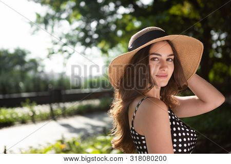Close-up Porttrait Of A Beautiful Young Brunette Woman Dressed In A Black Dress And A Hat With Wide 