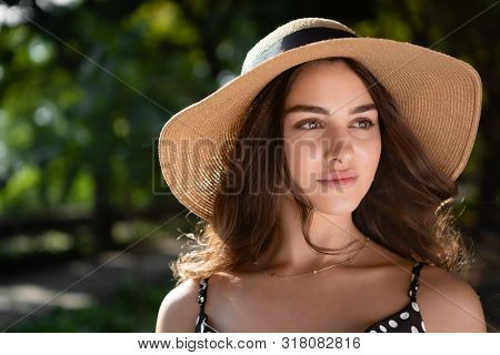Close-up Porttrait Of A Beautiful Young Brunette Woman Dressed In A Black Dress And A Hat With Wide 