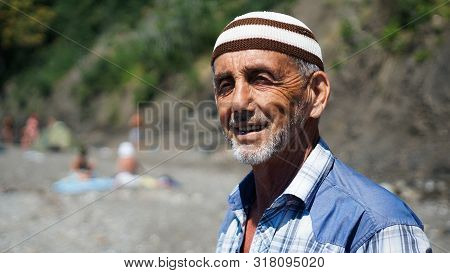 Old Man On The Beach. Cheerful Sunburnt Man Smiling And Squinting Enjoying Long Warm Vacation.