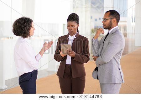Serious Female Professional Checking Report On Tablet During Meeting. Her Multiethnic Male And Femal