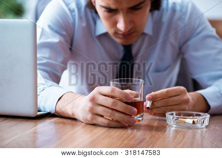 Male employee drinking alcohol and smoking cigarettes at workpla