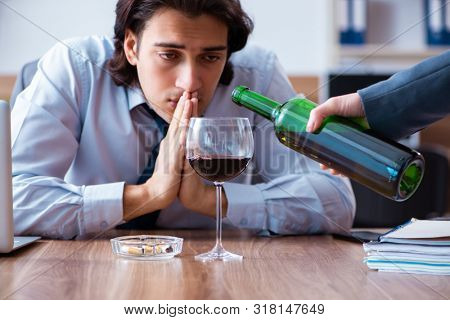 Male employee drinking alcohol and smoking cigarettes at workpla