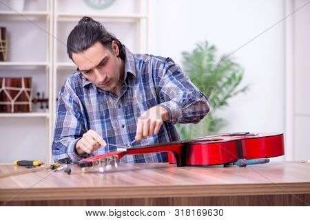 Young handsome repairman repairing guitar