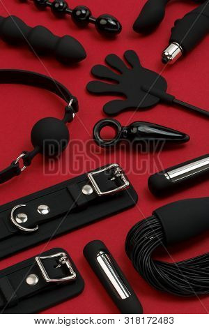 Various Rubber Sex Toys (dildo, Butt Plug, Whip, Vibrator, Gag, Bracelet) On A Red Background. Image