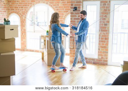 Young couple moving to a new home, having fun riding a skateboar
