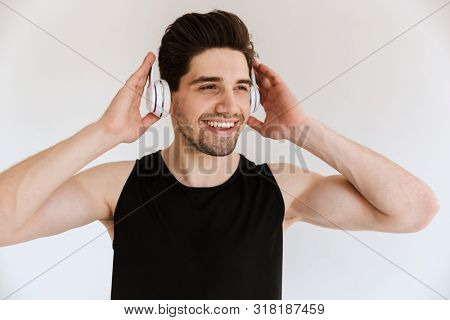 Photo of a handsome optimistic smiling sports man isolated over white wall background listening music with headphones.