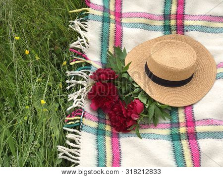 A Bouquet Of Red Peonies Under The Straw Hat On The Blanket. Picnic Concept. Copy Space