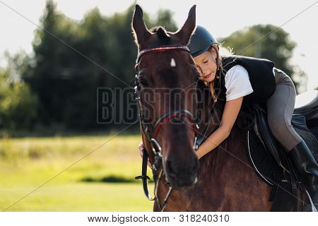 Girl Teenager Jockey Sits On A Brown Horse, Hugs And Strokes Her.