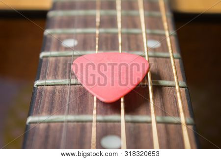 Red Pick On Acoustic Guitar String And Fingerboard Or Fretboard In Zoom View