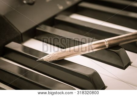 Old Pencil On Black Keys Of Electric Piano In Crosswise View. Concept About Piano Playing Or Piano L