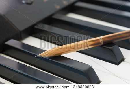 Old Pencil On Black Keys Of Electric Piano In Crosswise View. Concept About Piano Playing Or Piano L
