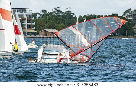 Child Sailing Competitors Climbing Back Into A Capsized Sailboat.  Children Sailing In Dinghies For 