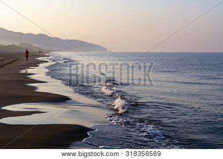 Unidentified Man Jogging In Orange Sportswear On Sandy Beach On Sinrise Over Sea Or Ocean