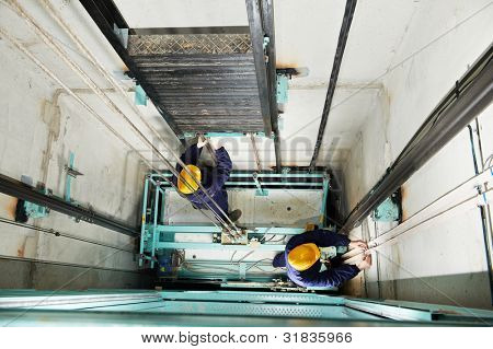 two machinist worker technicians at work adjusting lift with spanners in elevator hoistway