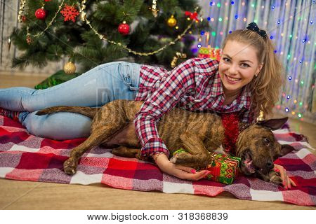 Merry Christmas And Happy New Year. A Charming Blonde Girl Lies Under The Christmas Tree And Plays W