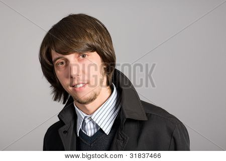 lächelnd junger Mann mit einem grauen Hintergrund.