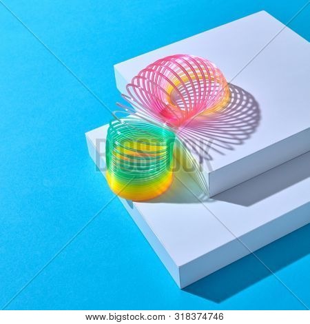Rainbow plastic multicolored spring spiral goes down white stairs step by step on a pastel background with shadows, copy space.