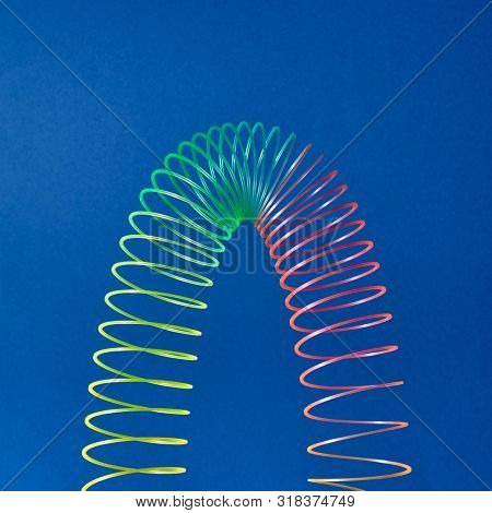 Stratching colorful toy spiral in the shape of parabola on a blue background with copy space.