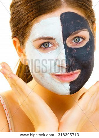 Woman With Clay Carbo Black Mask On Half Face And White Mud On Second Half. Girl Taking Care Of Oily