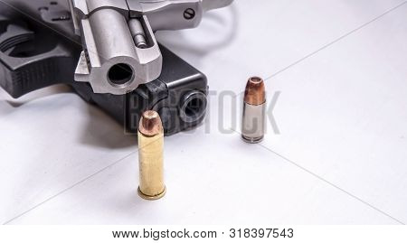 A Snub Nosed, Stainless 357 Magnum Revolver On Top Of A Black 9mm Pistol With A Bullet For Each Cali