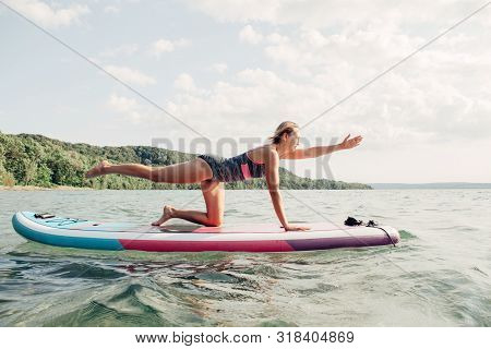 Middle Age Caucasian Woman Practising Yoga On Paddle Sup Surfboard At Sunset. Female Stretching Doin
