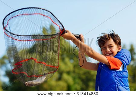 Beaming Dark-haired Boy Holding Fishing Net With Fish