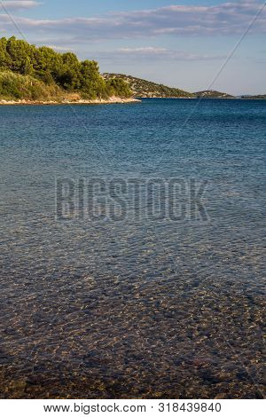 Empty Beach With Rocky Coast. Blue Clean Water Of The Adriatic Sea With Small Waves. Hill With A For