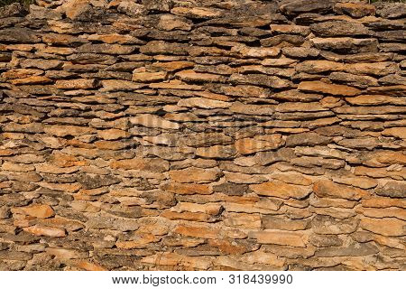 Stone Wall Made Of Various Natural Tones Of A Brown Color, Located Outdoors, Enlighted By Sunlight. 
