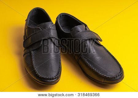 Black Childrens School Shoes With Velcro On A Yellow Background.