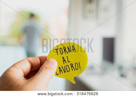 closeup of a man at the office with a note in his hand, with the text torna al lavoro, back to work written in italian, and a man seen behind standing in the background