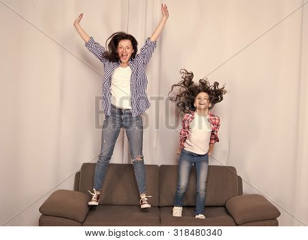Happy Family Celebrating Mothers Day. Happy Mother And Daughter Jumping On Sofa. Mother And Child En