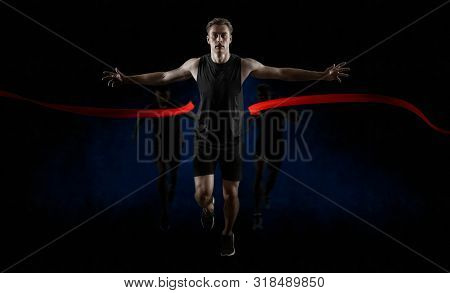 Runner wins by crossing the finish line.  Strong athletic man, running on dark background wearing in sportswear. Sport and fitness motivation