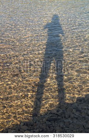 Shallow Water Of The Adriatic Sea Beach, With Stones Bottom. Silhouette Of A Woman (author), Long Ha