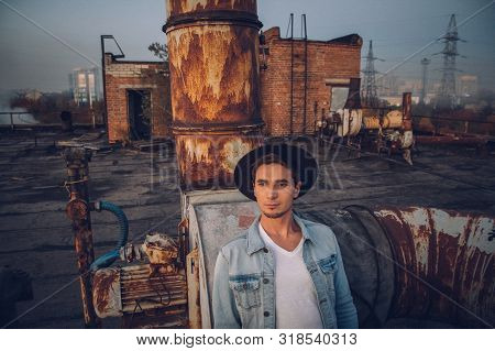 Urban Man With Hat Against The Background Of The City. Wearing White Shirt And Jeans. Old Neglected 