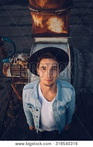 Urban Man With Hat Against The Background Of The City. Wearing White Shirt And Jeans. Old Neglected 