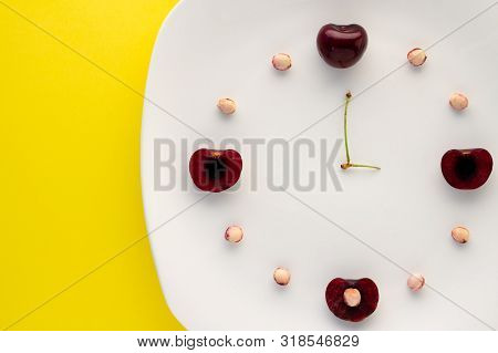 Close Up Of Red Cherries And Pits On A White Plate Showing The Time.