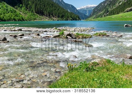 Fast Water Stream Flow Into Mountain Lake. Landscape With Stones In Brook Surrounded By Rich Vegetat