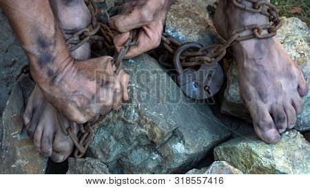 Hands And Feet Of A Slave Entangled In Iron Chains. An Attempt To Break Free From Slavery. The Symbo
