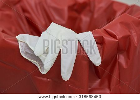 Close-up View Of A Used Surgical Disposable Glove On The Edge Of Red Garbage Bin In Operating Room