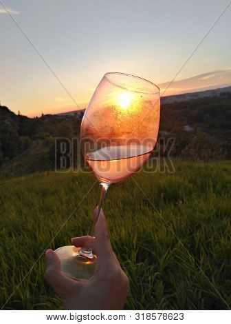 Wine Swirl With A Sky And Sunset. Wineglass With Woman Hand Swirling Rose Red Drink Outdoor During H